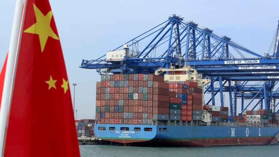 在中国天津的天津港集团有限公司码头，一艘船只驶过正在卸货的集装箱，上面飘扬着中国国旗